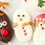 Close up of a Nutter Butter Snowman cookie pop with sanding sugar, pretzel arms, and candy decorations next to reindeer and Santa cookie pops.