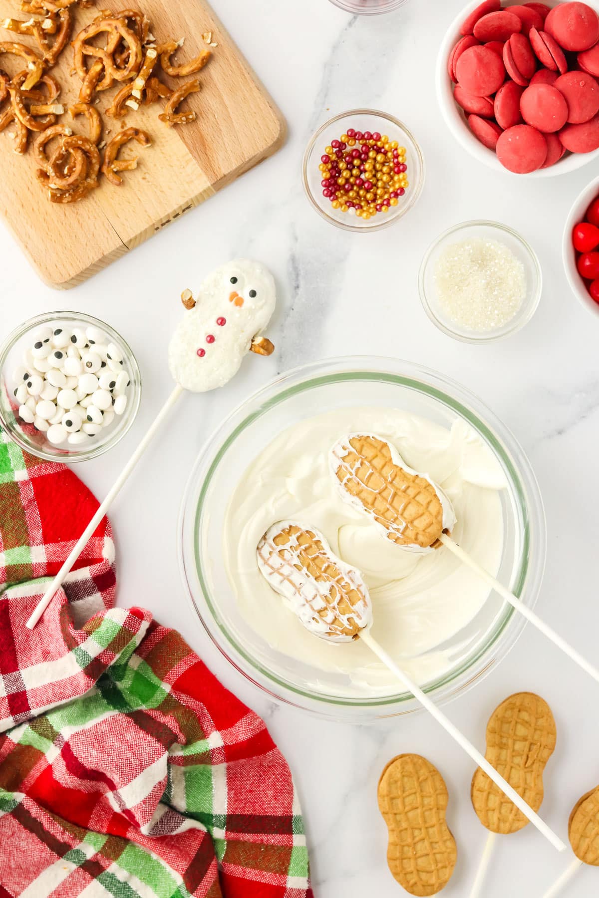 Nutter Butter cookie pops being dipped into melted white chocolate with a finished snowman cookie nearby.