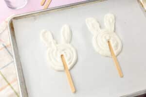 Popsicle sticks inserted into bunny-shaped yogurt pops on a parchment-lined baking sheet.