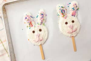 Two Easter bunny frozen yogurt pops on a baking sheet with coconut coating, sprinkles, and chocolate chip eyes.