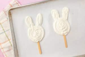 Two Easter bunny yogurt pops piped into shape on a baking sheet before adding toppings.