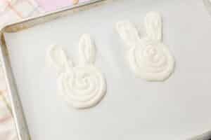 Bunny-shaped yogurt pops piped onto a parchment-lined baking sheet before inserting popsicle sticks.