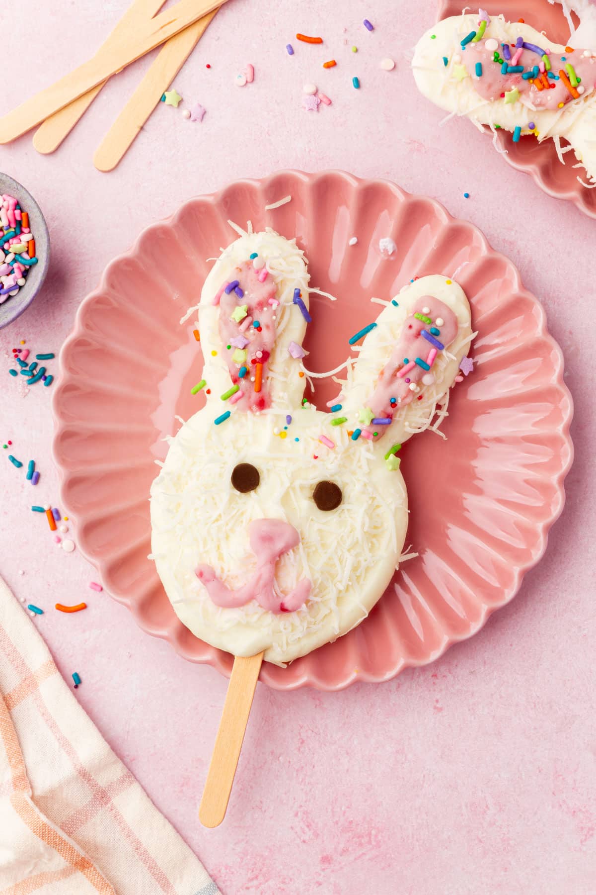 Easter bunny frozen yogurt pop decorated with coconut and sprinkles on a pink plate.