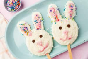Two Easter bunny frozen yogurt pops decorated with coconut and sprinkles on a blue plate.